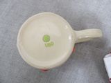 a white cup with a green dot on it next to a red and white checkered cloth