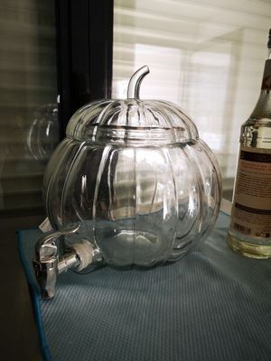 un bocal en verre contenant une citrouille, posé sur une table à côté d'une bouteille d'alcool