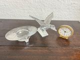 a glass bird figurine next to a clock on a wooden table