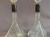 pair of clear glass perfume bottles with black tops on a white background