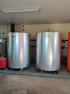 trois grandes cuves métalliques dans un garage, à côté de fûts orange