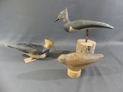 three carved birds are sitting on a wooden stand on a gray background