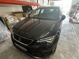 Une voiture noire est garée dans un garage, avec d'autres véhicules en arrière-plan.