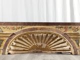 Un vieux ventilateur en bois est posé par terre devant un rideau blanc.