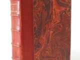 an old book with a red cover sitting on top of a white surface