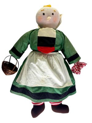 une poupée en peluche vêtue d'une robe verte et tenant un panier