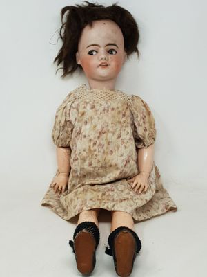 une poupée à l'ancienne, assise sur une surface blanche, vêtue d'une robe et de chaussures