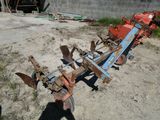 une charrue tractée posée dans la terre devant un bâtiment