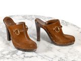 une paire de sabots en cuir marron posés sur une table en marbre, sur fond blanc