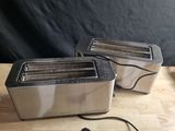 two silver toasters sitting on top of a wooden table next to a black backdrop