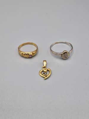 trois bagues en or et un pendentif en forme de cœur sur un fond blanc