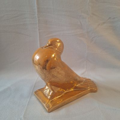 une statue d'oiseau dorée posée sur un socle, sur fond blanc