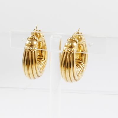 une paire de boucles d'oreilles créoles dorées posées sur un présentoir en acrylique transparent
