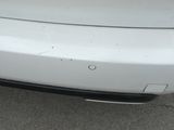 the rear end of a white car with scratches on it ' s bumper