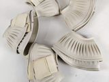 trois paires de chaussures blanches ornées de nœuds, posées sur une surface blanche
