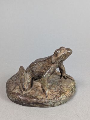 statue d'une grenouille assise sur un rocher, posée sur une surface blanche