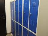 Plusieurs casiers bleus sont alignés dans un couloir, à côté d'une porte noire.