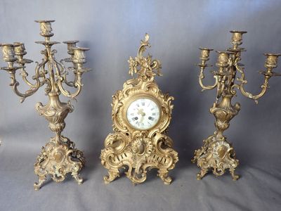 trois chandeliers anciens en laiton et une horloge sur fond gris