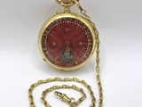 une montre de poche rouge avec une chaîne en or sur un fond blanc