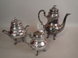 three pieces of silver tea and coffee set on a white surface