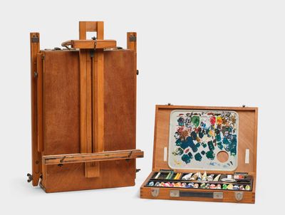 une image représentant un chevalet en bois sur lequel est posé un tableau, ainsi qu'une boîte de peinture
