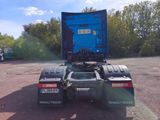 a blue semi truck parked in a lot with trees in the background