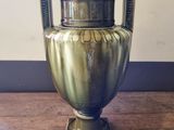 a gold vase on a wooden table with a striped wall in the background