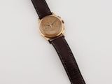 a gold watch with a brown leather strap on a white surface