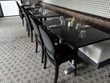 Dans un restaurant dont l'un des murs est recouvert de papier peint, des tables et des chaises sont alignées.