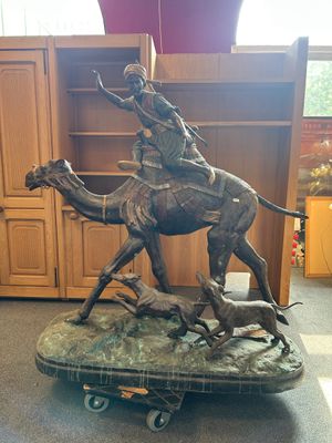 statue of a man riding a camel with a dog on a cart