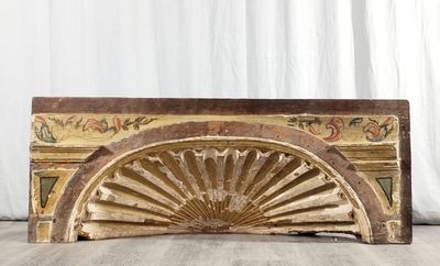 Un vieux ventilateur en bois est posé par terre devant un rideau blanc.