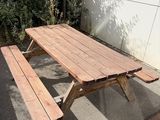 une table de pique-nique en bois avec deux bancs, devant un mur blanc