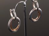 a pair of silver and gold hoop earrings on a black stand