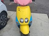 brightly colored motor scooter parked in parking lot next to parked cars