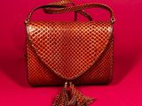 a brown snake skin purse with a tassel on a pink background
