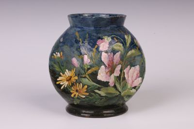 un vase avec des fleurs peintes dessus, posé sur une table