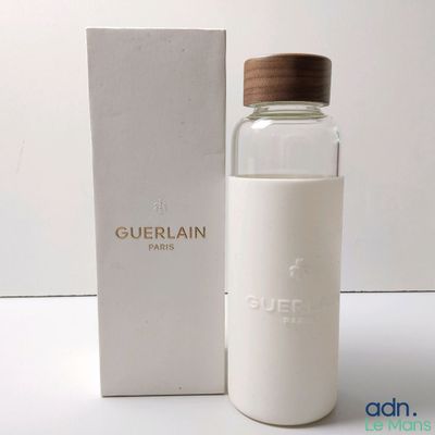un flacon d'eau de Guerlain avec un bouchon en bois, posé devant une boîte blanche