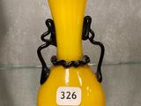 un vase jaune muni d'une anse noire, posé sur une étagère en verre