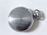 a silver pocket watch on a white surface with writing on it