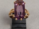 une image représentant une bague ornée d'une pierre violette posée sur un socle noir