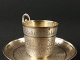 une tasse et une soucoupe argentées posées sur une soucoupe, sur un fond noir