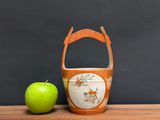 a green apple next to an orange vase on a wooden table