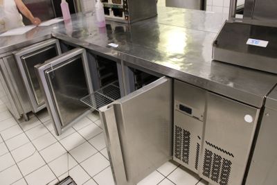 plan de travail en acier inoxydable dans une cuisine professionnelle, avec une femme debout à l'arrière-plan
