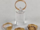 trois bagues en or et un récipient en verre posés sur une surface blanche