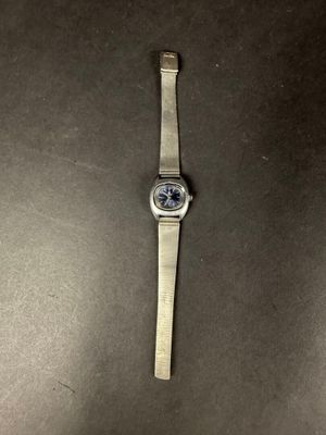 une montre en argent posée sur une table, à côté d'une table noire