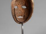 an image of a wooden mask on a metal stand on a gray background