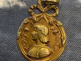 une vieille médaille en or sur laquelle est représenté le visage d'un homme, posée sur un tissu bleu