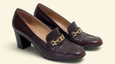 La femme porte une paire de chaussures marron ornées d'une chaîne dorée au talon.