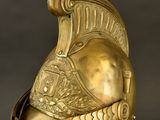 an antique gold helmet on a clear stand against a black background