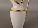 a white and gold pitcher with a handle on a table